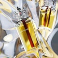 Lattafa Dynasty Lattafa 100ml EDP Unisex — A maroon textured box with a white ornate crest sits next to a clear glass perfume bottle topped with a silver crown-shaped cap with red accents.