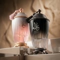 Zimaya Ghali Elegant Eau De Parfum 100ml by Zimaya — A pink patterned box with building facade design stands next to a fluted glass perfume bottle with a gold base and a pink tassel on the cap. | Zimaya Ghali Elegant Eau De Parfum 100ml oleh Zimaya — Peti merah jambu bercorak dengan reka bentuk fasad bangunan berdiri