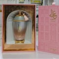Zimaya Ghali Elegant Eau De Parfum 100ml by Zimaya — A pink patterned box with building facade design stands next to a fluted glass perfume bottle with a gold base and a pink tassel on the cap. | Zimaya Ghali Elegant Eau De Parfum 100ml oleh Zimaya — Peti merah jambu bercorak dengan reka bentuk fasad bangunan berdiri
