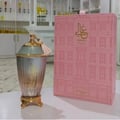 Zimaya Ghali Elegant Eau De Parfum 100ml by Zimaya — A pink patterned box with building facade design stands next to a fluted glass perfume bottle with a gold base and a pink tassel on the cap. | Zimaya Ghali Elegant Eau De Parfum 100ml oleh Zimaya — Peti merah jambu bercorak dengan reka bentuk fasad bangunan berdiri
