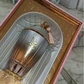 Zimaya Ghali Elegant Eau De Parfum 100ml by Zimaya — A pink patterned box with building facade design stands next to a fluted glass perfume bottle with a gold base and a pink tassel on the cap. | Zimaya Ghali Elegant Eau De Parfum 100ml oleh Zimaya — Peti merah jambu bercorak dengan reka bentuk fasad bangunan berdiri