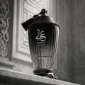 Zimaya Ghali Imperial Eau De Parfum — A dark grey textured box with a building facade pattern stands next to a dark, fluted perfume bottle with a tassel. | Zimaya Ghali Imperial Eau De Parfum — Kotak kelabu gelap bertekstur dengan corak fasad bangunan berdiri di sebelah botol minyak wangi gelap berlekuk dengan juntai.