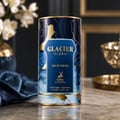 Maison Alhambra Glacier Flora 100ml Maison Alhambra — A blue perfume bottle with a gold cap and vertical gold lines on the glass, stands next to its matching cylindrical blue and gold patterned box on a white background. | Maison Alhambra Glacier Flora 100ml Maison Alhambra — Botol minyak wangi biru dengan penutup