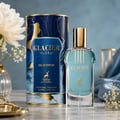 Maison Alhambra Glacier Flora 100ml Maison Alhambra — A blue perfume bottle with a gold cap and vertical gold lines on the glass, stands next to its matching cylindrical blue and gold patterned box on a white background. | Maison Alhambra Glacier Flora 100ml Maison Alhambra — Botol minyak wangi biru dengan penutup