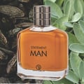 Grandeur Statement Man Eau De Parfum 100ml — A clear glass perfume bottle with amber liquid, a silver ribbed cap, and black text reading 'STATEMENT MAN' and a logo | Grandeur Statement Man Eau De Parfum 100ml — Botol minyak wangi kaca jernih dengan cecair berwarna ambar, penutup perak berjalur, dan teks hitam bertulis
