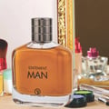Grandeur Statement Man Eau De Parfum 100ml — A clear glass perfume bottle with amber liquid, a silver ribbed cap, and black text reading 'STATEMENT MAN' and a logo | Grandeur Statement Man Eau De Parfum 100ml — Botol minyak wangi kaca jernih dengan cecair berwarna ambar, penutup perak berjalur, dan teks hitam bertulis