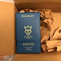 Bujairami Hectic — Clear faceted glass perfume bottle with blue cap next to blue presentation box with gold logo