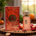 Paris Corner Khair Fusion Her 100ml — Red and gold patterned box next to a frosted pink perfume bottle with a gold textured cap. | Paris Corner Khair Fusion Her 100ml — Kotak corak merah dan emas di sebelah botol minyak wangi merah jambu beku dengan penutup bertekstur emas.