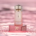 Paris Corner Khair Fusion Her 100ml — Red and gold patterned box next to a frosted pink perfume bottle with a gold textured cap. | Paris Corner Khair Fusion Her 100ml — Kotak corak merah dan emas di sebelah botol minyak wangi merah jambu beku dengan penutup bertekstur emas.