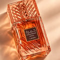 Lattafa Khamrah Mira by Lattafa EDP Unisex — Amber glass perfume bottle with a textured cap, next to its pink and blue watercolor-style box with gold accents.
