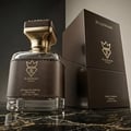 Bujairami Kingsman — A clear glass perfume bottle with a black leather band and gold accents sits next to its dark brown