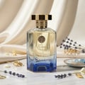 Maison Alhambra Kismet Lunar Magic 100ml — A clear glass perfume bottle with a gold cap and blue gradient base sits next to its matching blue and gold box on a white background. | Maison Alhambra Kismet Lunar Magic 100ml — Botol minyak wangi kaca jernih dengan penutup emas dan tapak gradien biru terletak di sebelah