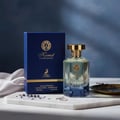 Maison Alhambra Kismet Lunar Magic 100ml — A clear glass perfume bottle with a gold cap and blue gradient base sits next to its matching blue and gold box on a white background. | Maison Alhambra Kismet Lunar Magic 100ml — Botol minyak wangi kaca jernih dengan penutup emas dan tapak gradien biru terletak di sebelah