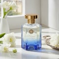 Maison Alhambra Kismet Lunar Magic 100ml — A clear glass perfume bottle with a gold cap and blue gradient base sits next to its matching blue and gold box on a white background. | Maison Alhambra Kismet Lunar Magic 100ml — Botol minyak wangi kaca jernih dengan penutup emas dan tapak gradien biru terletak di sebelah