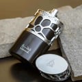 Lattafa Qimmah Eau De Parfum for Men 100ml — A black perfume box with a clear plastic overlay featuring a black and silver giraffe-like pattern sits next to a matching black perfume bottle with a silver, patterned cage-like cap. | Lattafa Qimmah Eau De Parfum for Men 100ml — Kotak minyak wangi hitam dengan lapisan