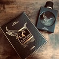 Lattafa Malik Al Tayoor Concentrated 100ml — Black perfume bottle and its black textured box with a golden eagle emblem and Arabic text, set against a white background. | Lattafa Malik Al Tayoor Concentrated 100ml — Botol minyak wangi hitam dan kotaknya yang bertekstur hitam dengan lambang helang emas dan teks Arab