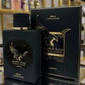 Lattafa Malik Al Tayoor Concentrated 100ml — Black perfume bottle and its black textured box with a golden eagle emblem and Arabic text, set against a white background. | Lattafa Malik Al Tayoor Concentrated 100ml — Botol minyak wangi hitam dan kotaknya yang bertekstur hitam dengan lambang helang emas dan teks Arab
