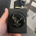 Lattafa Malik Al Tayoor Concentrated 100ml — Black perfume bottle and its black textured box with a golden eagle emblem and Arabic text, set against a white background. | Lattafa Malik Al Tayoor Concentrated 100ml — Botol minyak wangi hitam dan kotaknya yang bertekstur hitam dengan lambang helang emas dan teks Arab