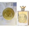 Ard Al Zaafaran Mithqal 100ml — A clear glass perfume bottle with gold liquid and a circular gold emblem, next to its white and gold patterned box with a matching emblem. | Ard Al Zaafaran Mithqal 100ml — Botol minyak wangi kaca jernih dengan cecair emas dan lambang emas bulat, bersebelahan dengan kotak corak putih
