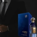Al Wataniah Muheeb Perfume Man by Al Wataniah 100ml — A dark blue perfume bottle with a gold cap sits next to its matching dark blue box with ornate gold Arabic calligraphy and floral designs. | Al Wataniah Muheeb Perfume Man by Al Wataniah 100ml — Botol minyak wangi biru gelap dengan penutup emas terletak di sebelah