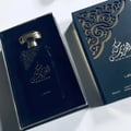 Lattafa Musk Al Aroos by Lattafa 80ml EDP — A black perfume box with gold ornate cutouts and Arabic calligraphy sits next to a dark glass perfume bottle with a gold cap and matching ornate design. | Lattafa Musk Al Aroos by Lattafa 80ml EDP — Kotak minyak wangi hitam dengan potongan berukir emas dan kaligrafi Arab