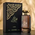 Lattafa Musk Al Aroos by Lattafa 80ml EDP — A black perfume box with gold ornate cutouts and Arabic calligraphy sits next to a dark glass perfume bottle with a gold cap and matching ornate design. | Lattafa Musk Al Aroos by Lattafa 80ml EDP — Kotak minyak wangi hitam dengan potongan berukir emas dan kaligrafi Arab