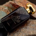 Lattafa Musk Al Aroos by Lattafa 80ml EDP — A black perfume box with gold ornate cutouts and Arabic calligraphy sits next to a dark glass perfume bottle with a gold cap and matching ornate design. | Lattafa Musk Al Aroos by Lattafa 80ml EDP — Kotak minyak wangi hitam dengan potongan berukir emas dan kaligrafi Arab