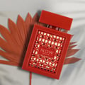 Rave Now Rouge Perfume EDP 100ml by RAVE — A red box with a geometric pattern sits next to an orange perfume bottle with a similar geometric cutout design. | Rave Now Rouge Perfume EDP 100ml by RAVE — Kotak merah dengan corak geometri terletak di sebelah botol minyak wangi oren dengan reka bentuk potongan geometri
