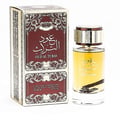 Ard Al Zaafaran Oud Al Turas — A clear glass perfume bottle with golden cap and a dark dried plant inside, next to a gold and maroon ornate box. | Botol minyak wangi kaca jernih dengan penutup emas dan tumbuhan kering gelap di dalamnya, bersebelahan dengan kotak berhias emas dan merah marun.