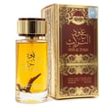 Ard Al Zaafaran Oud Al Turas — A clear glass perfume bottle with golden cap and a dark dried plant inside, next to a gold and maroon ornate box. | Botol minyak wangi kaca jernih dengan penutup emas dan tumbuhan kering gelap di dalamnya, bersebelahan dengan kotak berhias emas dan merah marun.