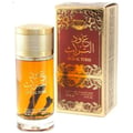 Ard Al Zaafaran Oud Al Turas — A clear glass perfume bottle with golden cap and a dark dried plant inside, next to a gold and maroon ornate box. | Botol minyak wangi kaca jernih dengan penutup emas dan tumbuhan kering gelap di dalamnya, bersebelahan dengan kotak berhias emas dan merah marun.