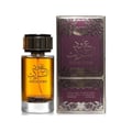 Ard Al Zaafaran Oud Al Turas — A clear glass perfume bottle with golden cap and a dark dried plant inside, next to a gold and maroon ornate box. | Botol minyak wangi kaca jernih dengan penutup emas dan tumbuhan kering gelap di dalamnya, bersebelahan dengan kotak berhias emas dan merah marun.