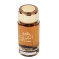 Ard Al Zaafaran Oud Al Turas — A clear glass perfume bottle with golden cap and a dark dried plant inside, next to a gold and maroon ornate box. | Botol minyak wangi kaca jernih dengan penutup emas dan tumbuhan kering gelap di dalamnya, bersebelahan dengan kotak berhias emas dan merah marun.