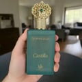 Teal perfume bottle with gold cap held in a hand, blurred indoor background