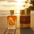 Perfume bottle broken, amber glow emerging; Langkawi beach at sunset Malaysia — clear bottle and box, cinematic lighting.