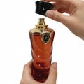 Hand holding a red perfume bottle with a gold cap against a white background