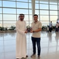 Two men standing in an airport terminal, one holding a trophy.