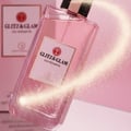 Glitz & Glam floating above mirror with vanilla stardust comet tail; soft pink glow; bottle and box clearly visible.