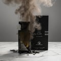 Oud Elixir Perfume Perfume bottle broken, fog emerging; studio on white marble Malaysia — clear bottle and box, cinematic lighting