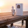 Lattafa Maahir Bottle & box placed on weathered teak pier by the sea at golden hour; ocean waves gently lapping; salt mist visible; sunrise/early morning light.