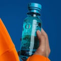 Hand holding a blue bottle with a brand logo against a blue background