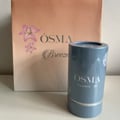Blue cylindrical product with 'OSMA' branding next to a pink 'OSMA Breeze' bag on a light background