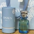 OSMA perfume bottle and cylindrical container on a textured surface with a decorative background