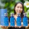 Set of blue perfume bottles with silver caps on a reflective surface, against a sky background.