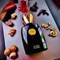 Black perfume bottle with gold cap on a reflective surface surrounded by nuts and leaves
