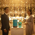 Rabab Blue 100ml -  Malaysian couple at arrivals with Luxe Journey bottle and box on marble plinth; warm light confetti; balanced unisex frame