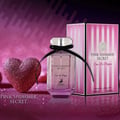 Maison Alhambra Pink Shimmer Secret 100ml — Pink perfume bottle with a black ribbon bow, next to its matching pink striped box, on a white background. | Maison Alhambra Pink Shimmer Secret 100ml — Botol minyak wangi merah jambu dengan reben hitam, bersebelahan kotak berjalur merah jambu yang sepadan, di atas latar