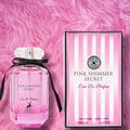 Maison Alhambra Pink Shimmer Secret 100ml — Pink perfume bottle with a black ribbon bow, next to its matching pink striped box, on a white background. | Maison Alhambra Pink Shimmer Secret 100ml — Botol minyak wangi merah jambu dengan reben hitam, bersebelahan kotak berjalur merah jambu yang sepadan, di atas latar