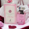 Maison Alhambra Pink Shimmer Secret 100ml — Pink perfume bottle with a black ribbon bow, next to its matching pink striped box, on a white background. | Maison Alhambra Pink Shimmer Secret 100ml — Botol minyak wangi merah jambu dengan reben hitam, bersebelahan kotak berjalur merah jambu yang sepadan, di atas latar