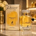 Maison Alhambra Precious Gold 80ml by Maison Alhambra — A gold-themed perfume box and bottle are displayed side-by-side against a white background. The box features abstract gold brushstrokes and a deer silhouette, while the bottle contains golden liquid and has a heart-shaped charm. | Maison Alhambra Precious Gold